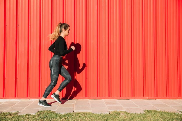 Free photo young woman running near red wall