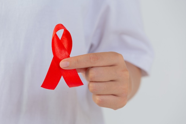 Young woman's hand holding red breast cancer and AIDS awareness ribbon