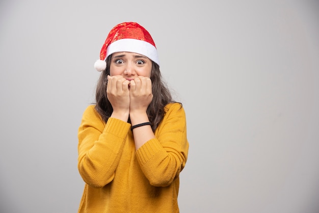 Young woman in Santa Claus red hat posing over a white wall. 