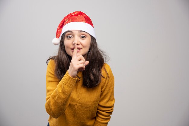 Young woman in Santa hat making silence sign. 