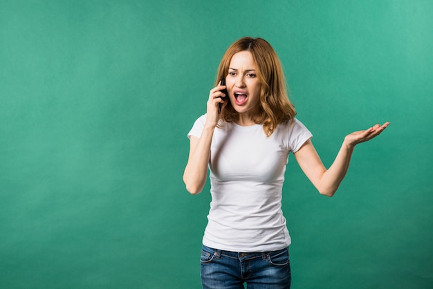 Free photo young woman screaming on smart phone against green backdrop