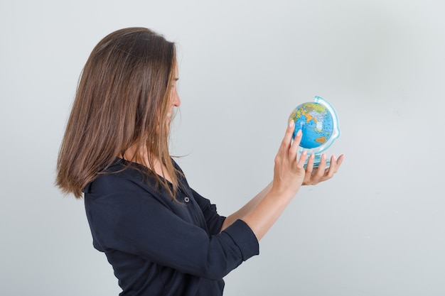 Free photo young woman searching for destination on globe in black shirt and looking cheerful .