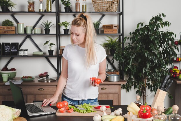 Young woman searching recipe on laptop in the kitchen