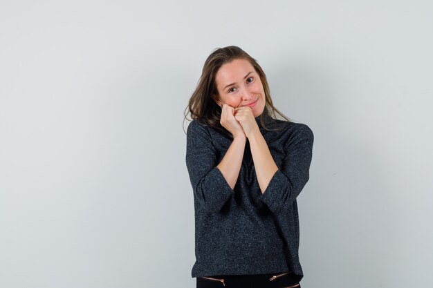 Young woman in shirt leaning cheek on fists and looking lovely 