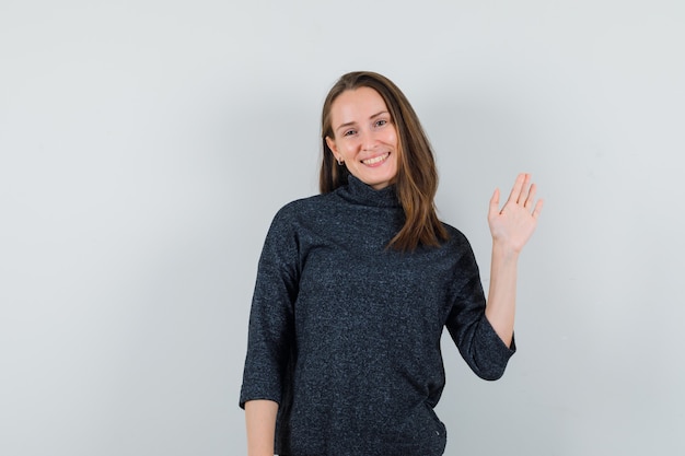 Young woman in shirt waving hand to say goodbye and looking cheerful 