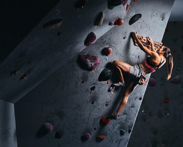 Young woman in shorts and sports bra exercising on a bouldering wall indoors.