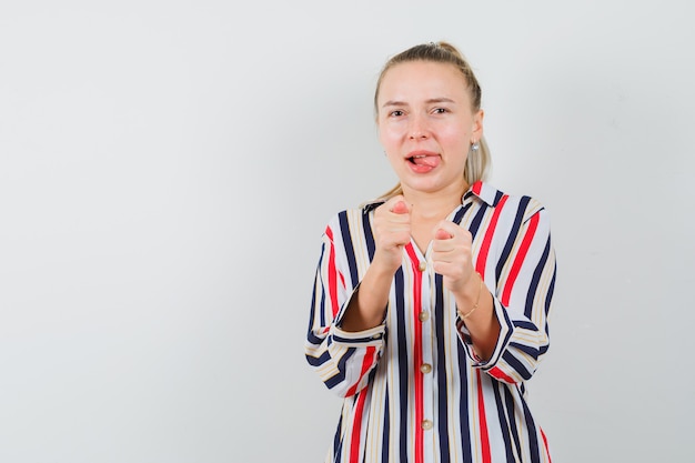 Young woman showing camera hand gesture in striped blouse and looking optimistic