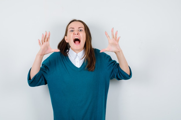 Young woman showing claws imitating a cat in sweater over white shirt and looking aggressive. front view.