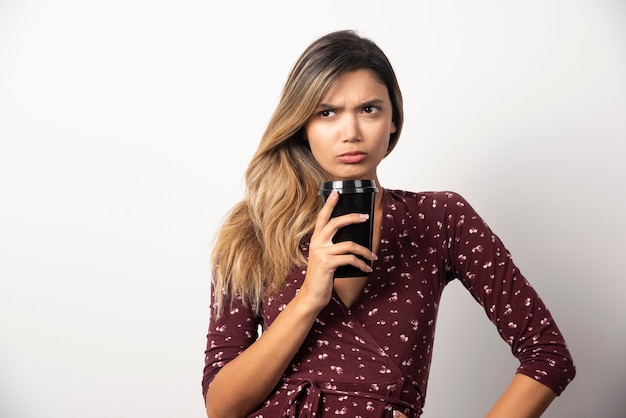 Young woman showing a cup of drink on white wall. 