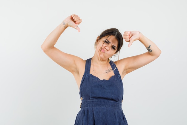 Young woman showing double thumbs down in dress and looking dissatisfied