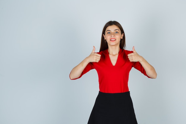 Free photo young woman showing double thumbs up in red blouse, black skirt and looking happy