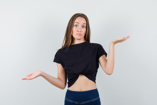 Young woman showing helpless gesture in black blouse and looking sorrowful