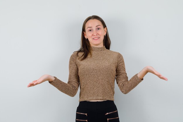 Young woman showing helpless gesture in golden blouse , front view.