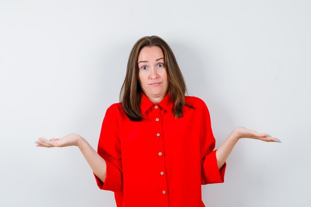 Young woman showing helpless gesture in red blouse and looking confused , front view.