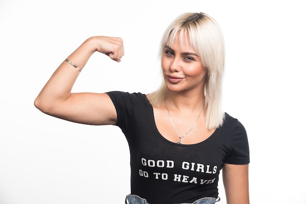 Free photo young woman showing muscles on white wall with happy expression.