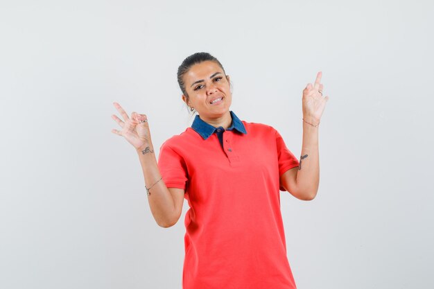 Young woman showing ok signs in red t-shirt and looking happy. front view.