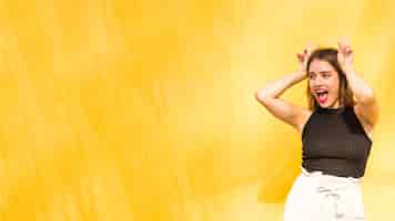 Free photo young woman showing peace sign over her head against yellow background