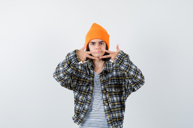 Young woman showing three fingers in orange hat and checkered shirt and looking unhappy