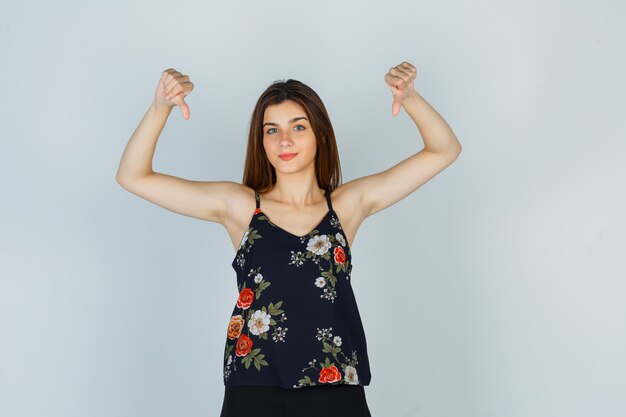 Young woman showing thumbs down in floral top and looking wistful