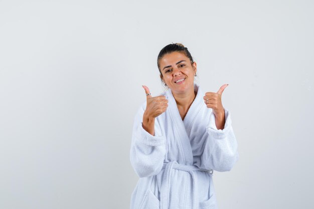 Young woman showing thumbs up in bathrobe and looking happy