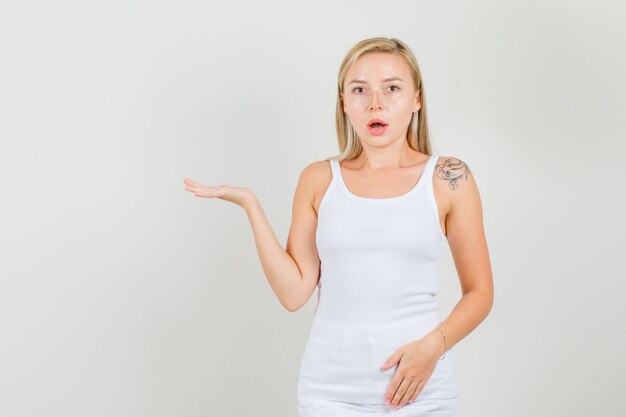 Young woman in singlet, mini skirt keeping open palm raised and looking surprised