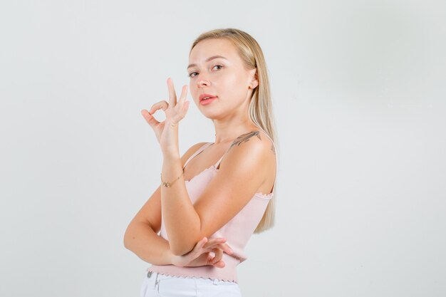 Young woman in singlet, mini skirt showing ok gesture and looking confident