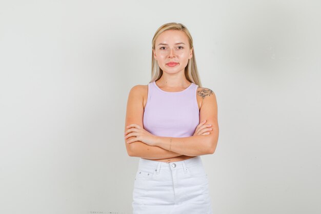 Young woman in singlet, mini skirt standing with crossed arms and looking confident