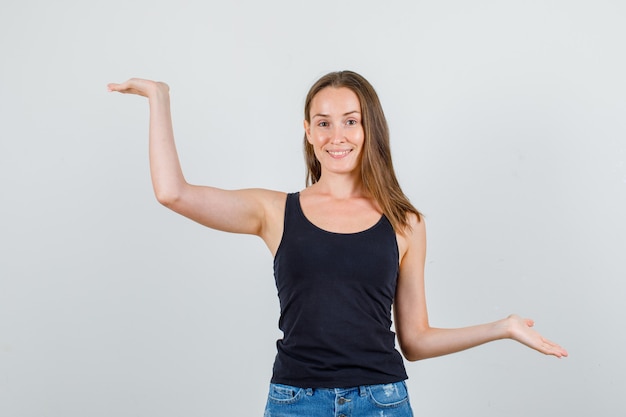 Young woman in singlet, shorts keeping palms open and looking cheery