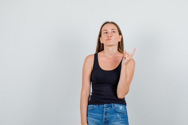 Young woman in singlet, shorts pointing away finger and looking thoughtful