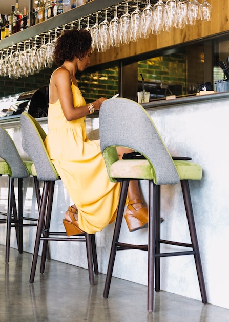 Free photo young woman sitting on bar stool using smartphone in the restaurant