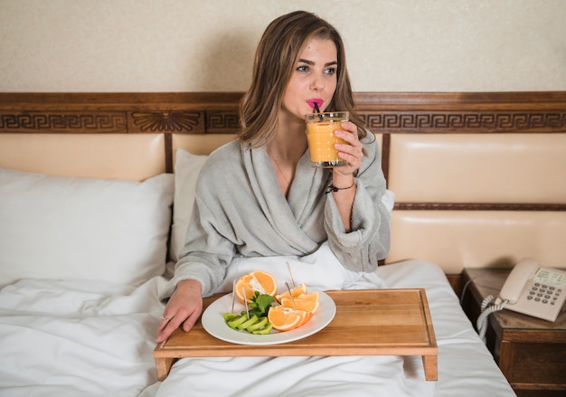 Free photo young woman sitting on bed drinking the glass of juice