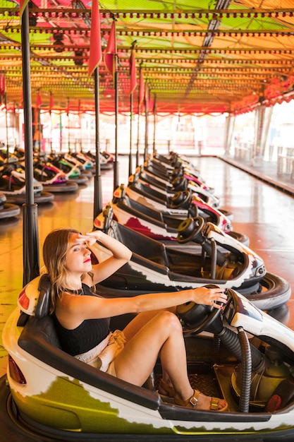 Young woman sitting in the bumper car shielding her eyes at amusement park