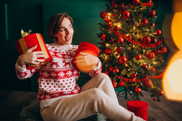 Young woman sitting by the Christmas tree with red boxes