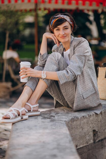 Young woman sitting by the fountain and drinking coffee