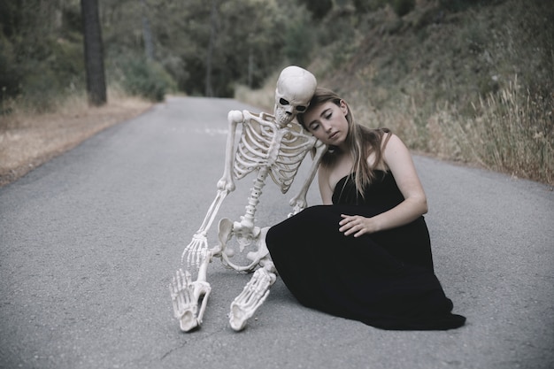 Free Photo young woman sitting on empty road with skeleton