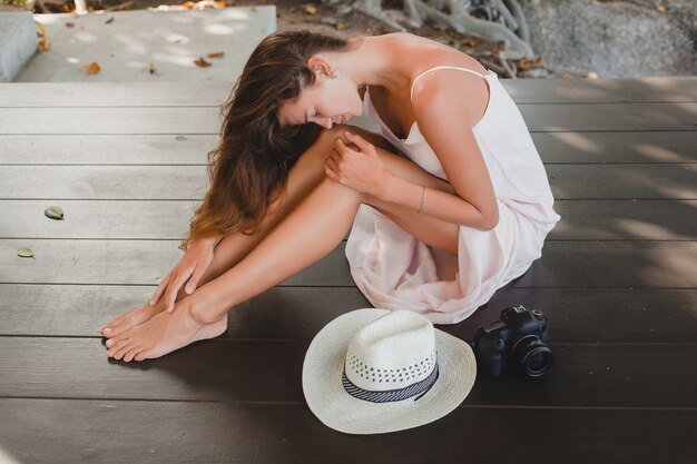 Young woman sitting on floor barefoot in pale dress, smiling, natural beauty, straw hat, digital camera, 