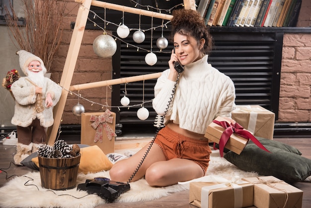 Free photo a young woman sitting on fluffy carpet and speaking on telephone