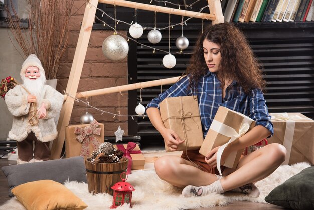 Young woman sitting on fluffy carpet with boxes of Christmas presents 