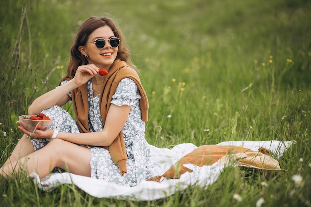 Young woman sitting on grass and eating strawberries