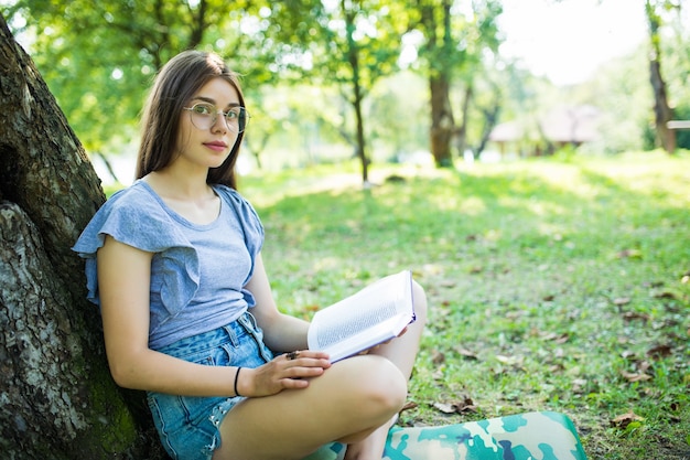 Young woman sitting and reading her favorite book on a o green gras under tree in a nice sunny summer