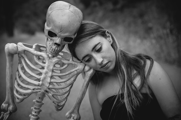 Free photo young woman sitting on road with skeleton and looking down