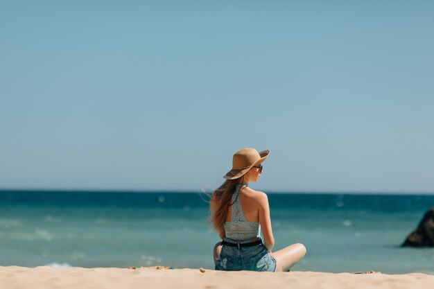 Young woman sitting on sand and looking to a sea. Rear view