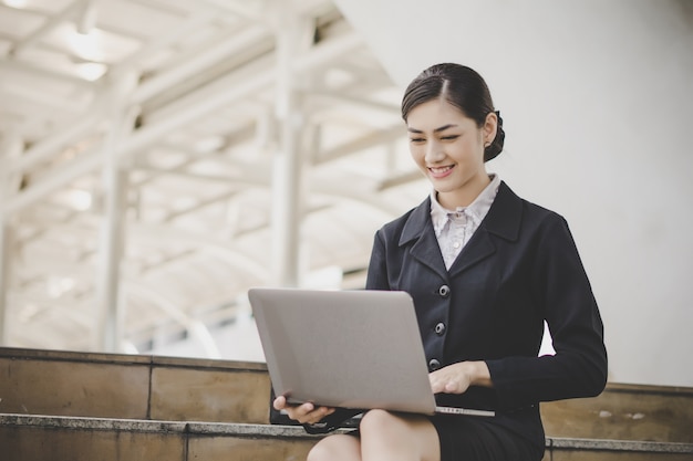 Young woman sitting on staircase using laptop computer. Female working on laptop in an outdoor