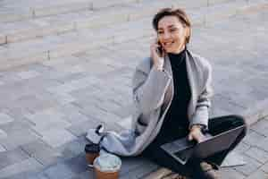 Free photo young woman sitting on stairs and working on computer