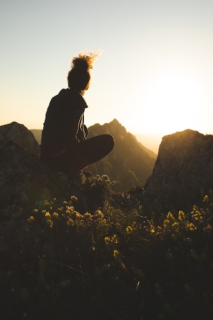 Free photo young woman sitting on top of the mountain and enjoying the view during sunset