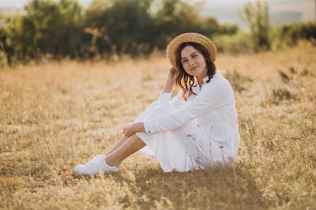 Young woman sitting in white dress and hat on the ground