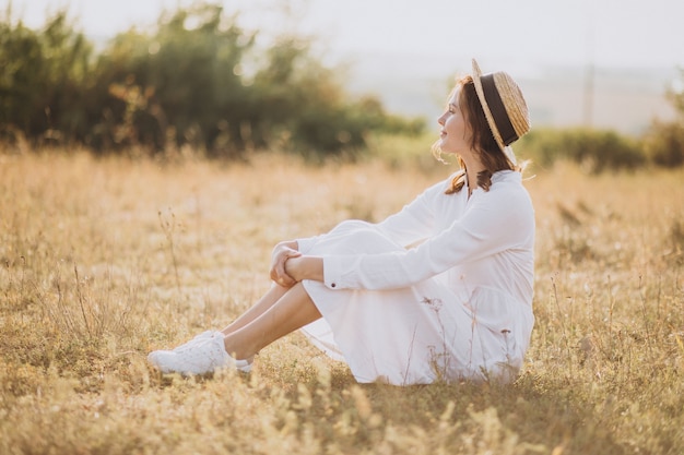 Free photo young woman sitting in white dress and hat on the ground