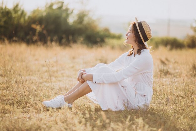 Young woman sitting in white dress and hat on the ground