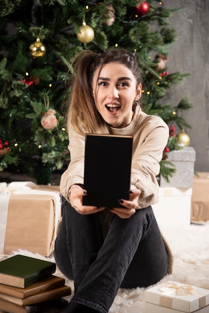 Free Photo young woman sitting with black notebook near christmas tree.