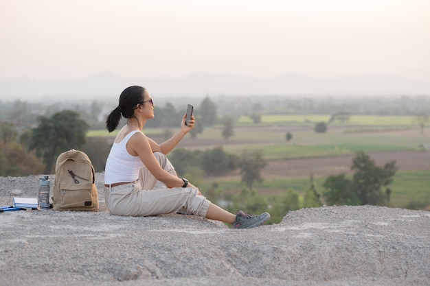 Free Photo young woman sitting with mobile phone. high mountains tourist path at sunset.